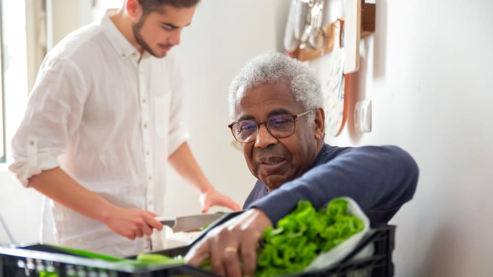 A Life Line volunteer handing a crate of fresh produce to an older Bronx resident at home