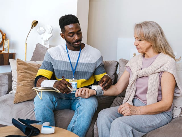 A community health worker checking a member's blood pressure during a home visit
