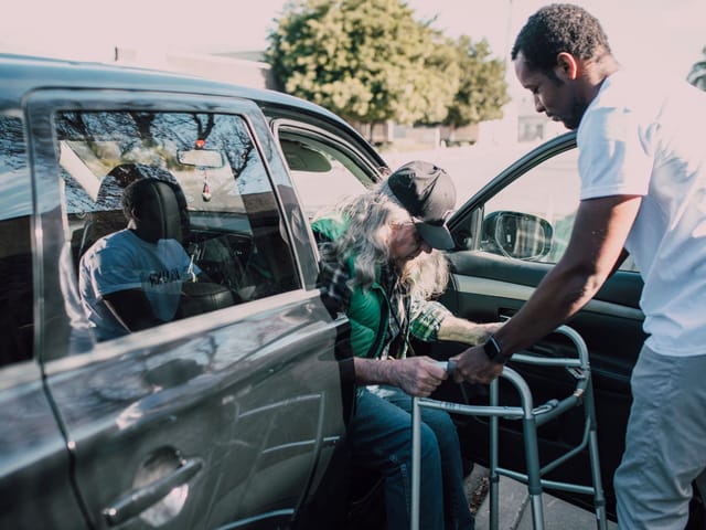 A member being helped out of a vehicle with a walker before an appointment